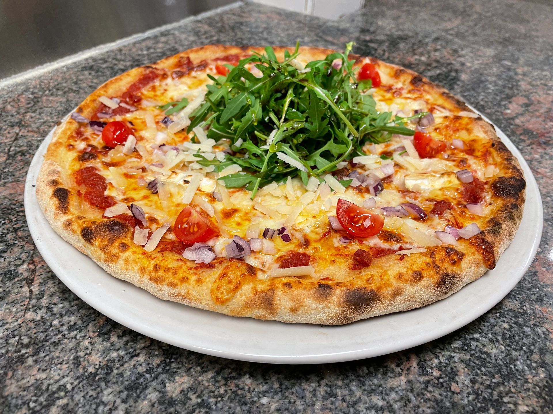 Une pizza garnie d'oignons rouges, tomates et roquette.