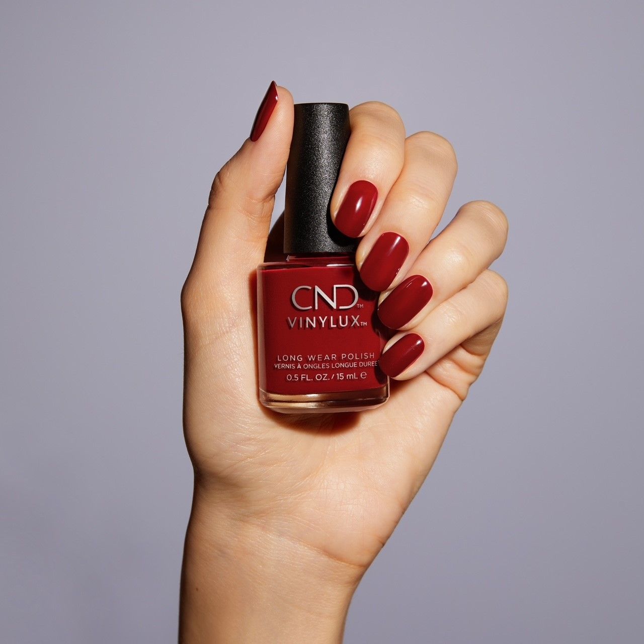 Eine Frauenhand hält eine Flasche CND Vinylux Nagellack in Dunkelrot