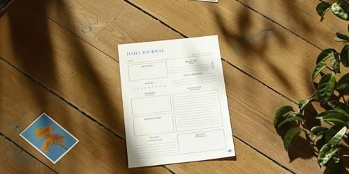 Un formulario blanco y una tarjeta azul sobre una mesa de madera junto a hojas de plantas verdes.