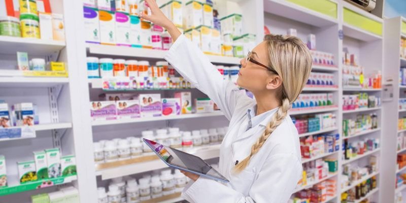 Una farmacéutica está mirando un frasco de medicamentos en una farmacia.