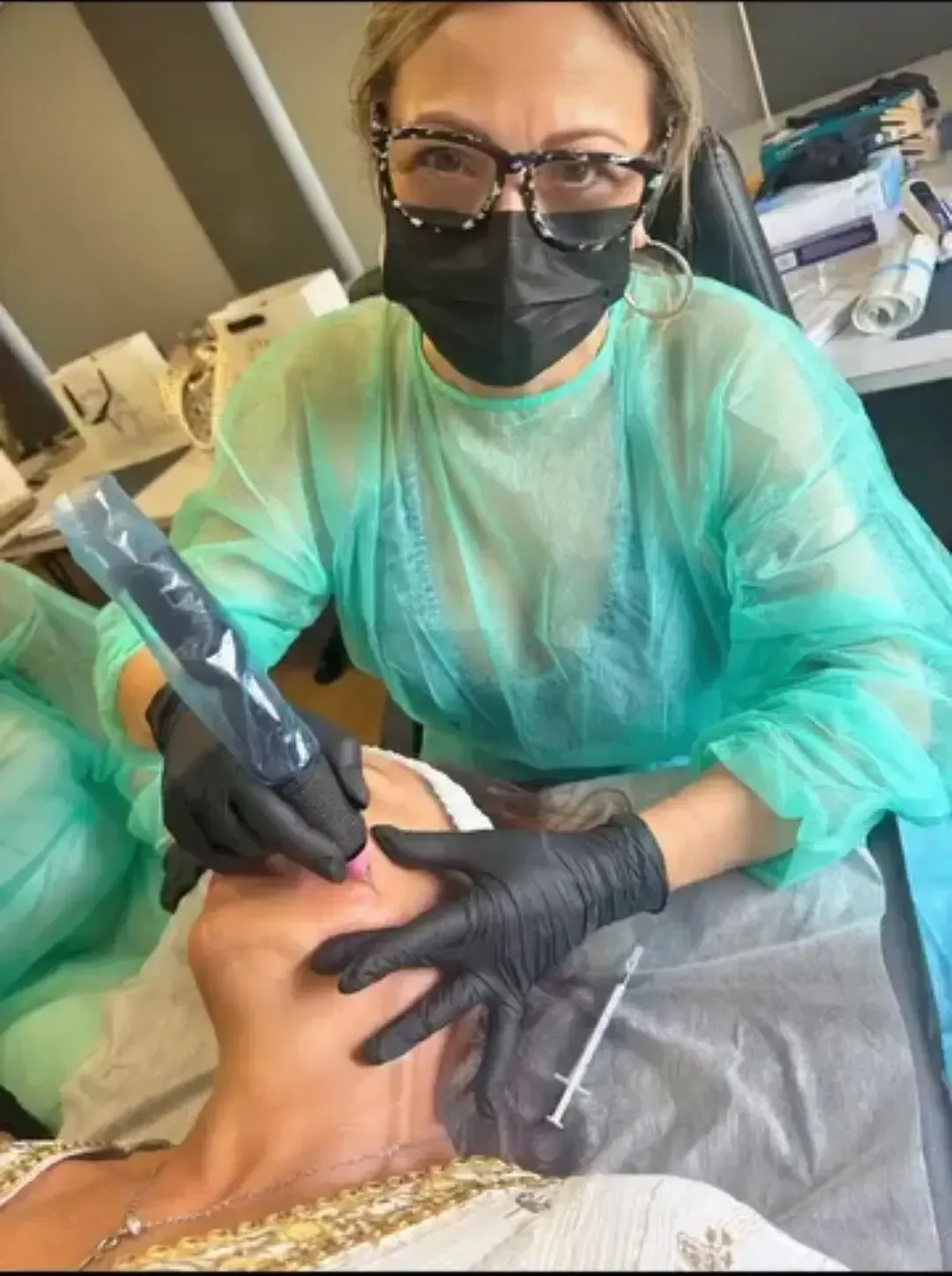 Profesional sanitario con mascarilla y guantes realizando un tratamiento a un paciente en una sala de consulta.