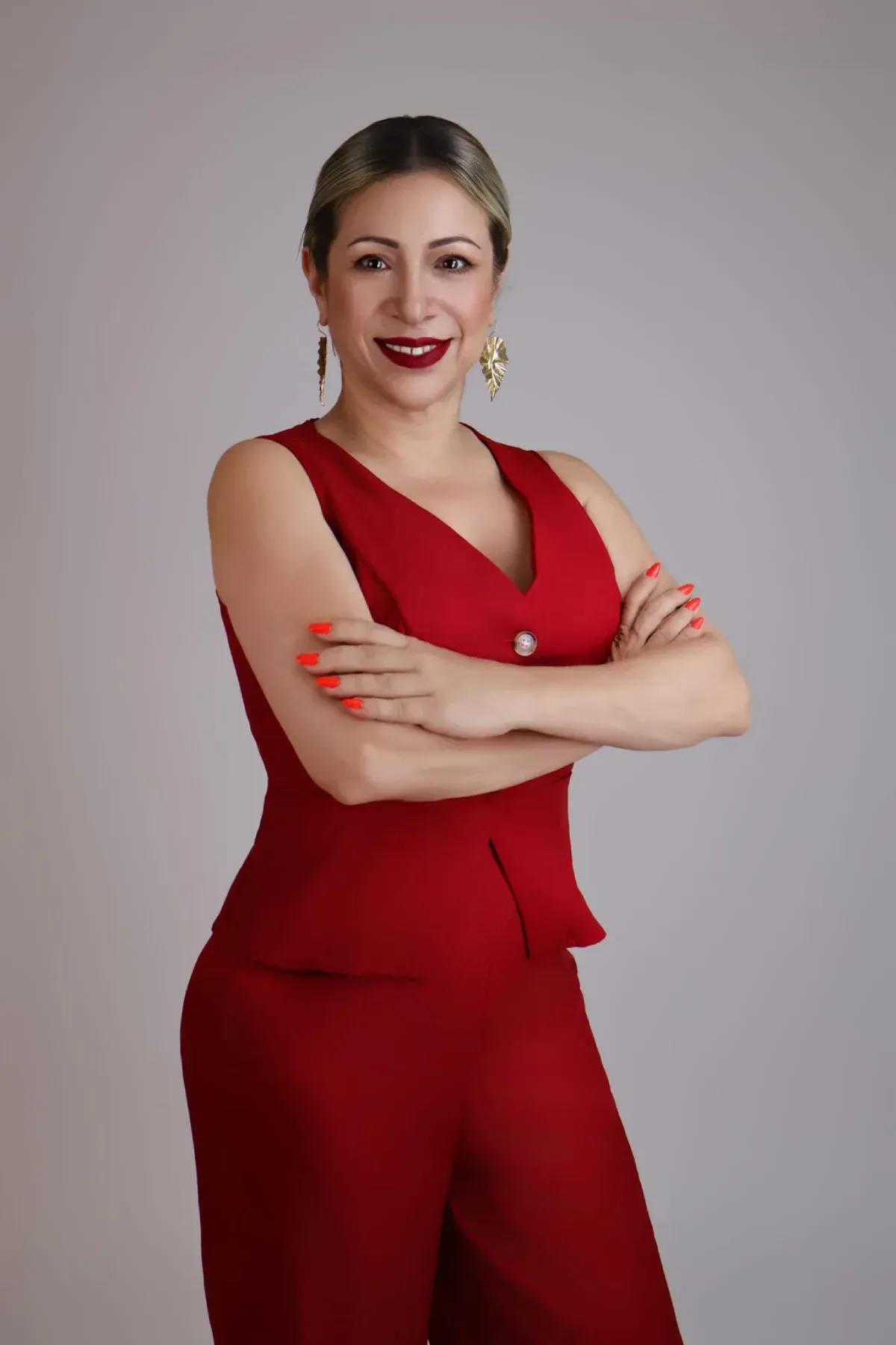 Mujer con un conjunto rojo sin mangas, de pie con los brazos cruzados sobre un fondo gris.