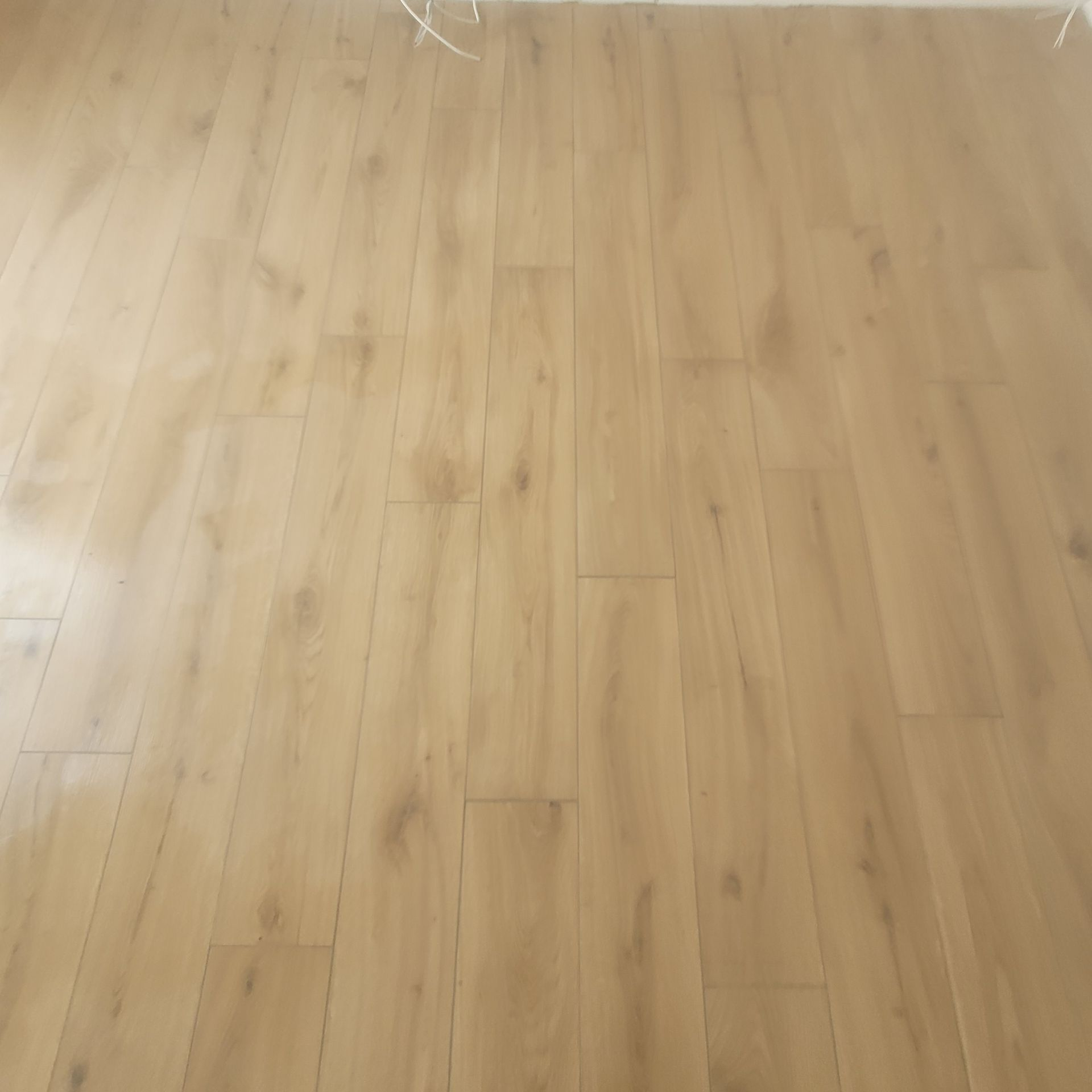 Plancher en bois clair avec un léger reflet et un mur blanc au bord supérieur