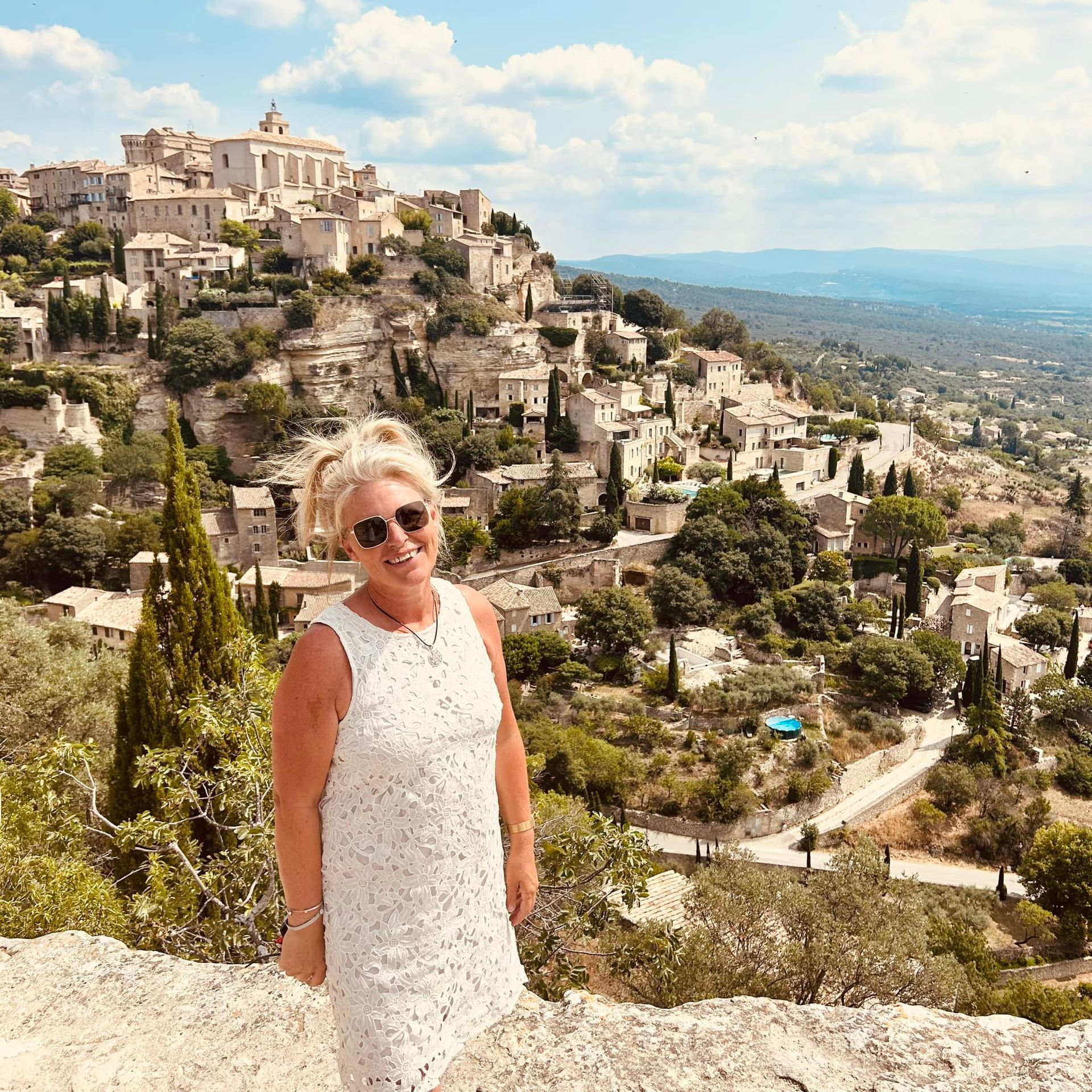 Flore en robe blanche se tient au sommet d'une colline surplombant une ville.