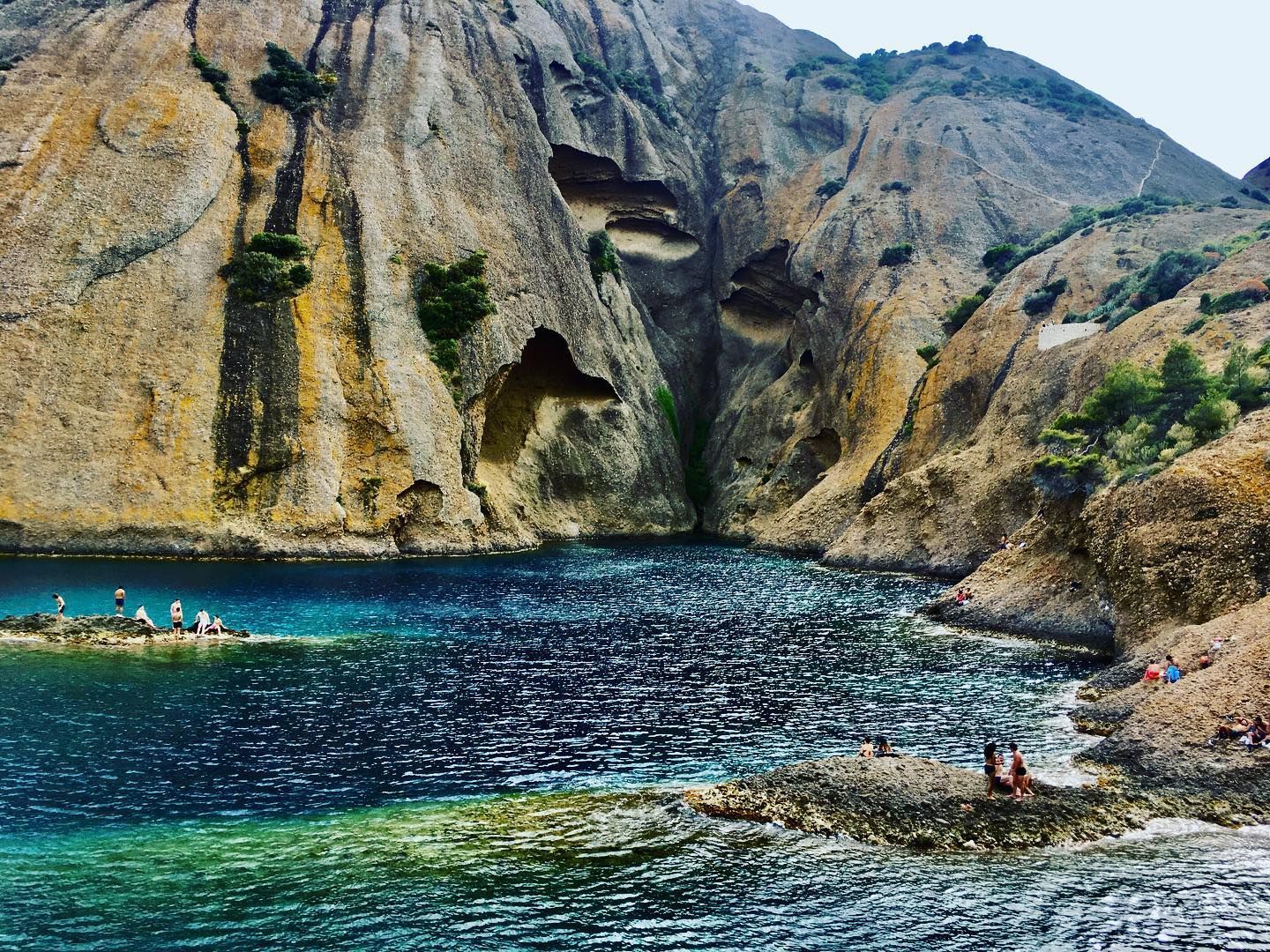 Crique turquoise avec des nageurs près d'une falaise rocheuse.