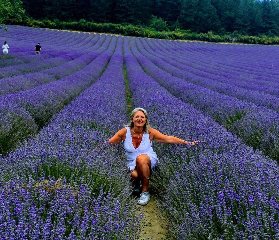Flore dans un champ de lavandes violettes, assise sur un chemin, les bras étendus.