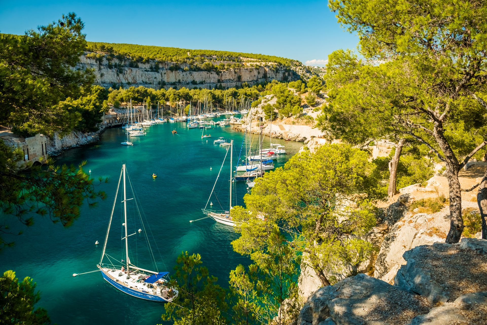 Crique turquoise avec des voiliers, des falaises rocheuses et des arbres sous un ciel d'un bleu éclatant