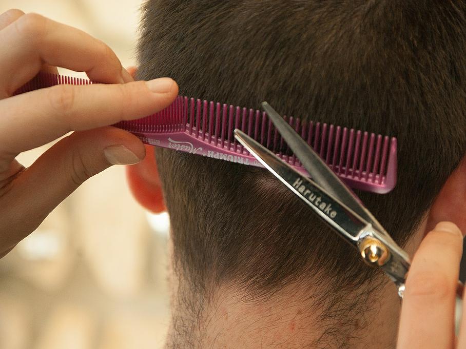 Coiffeuse coupant l'arrière des cheveux d'un homme avec un peigne et des ciseaux roses.