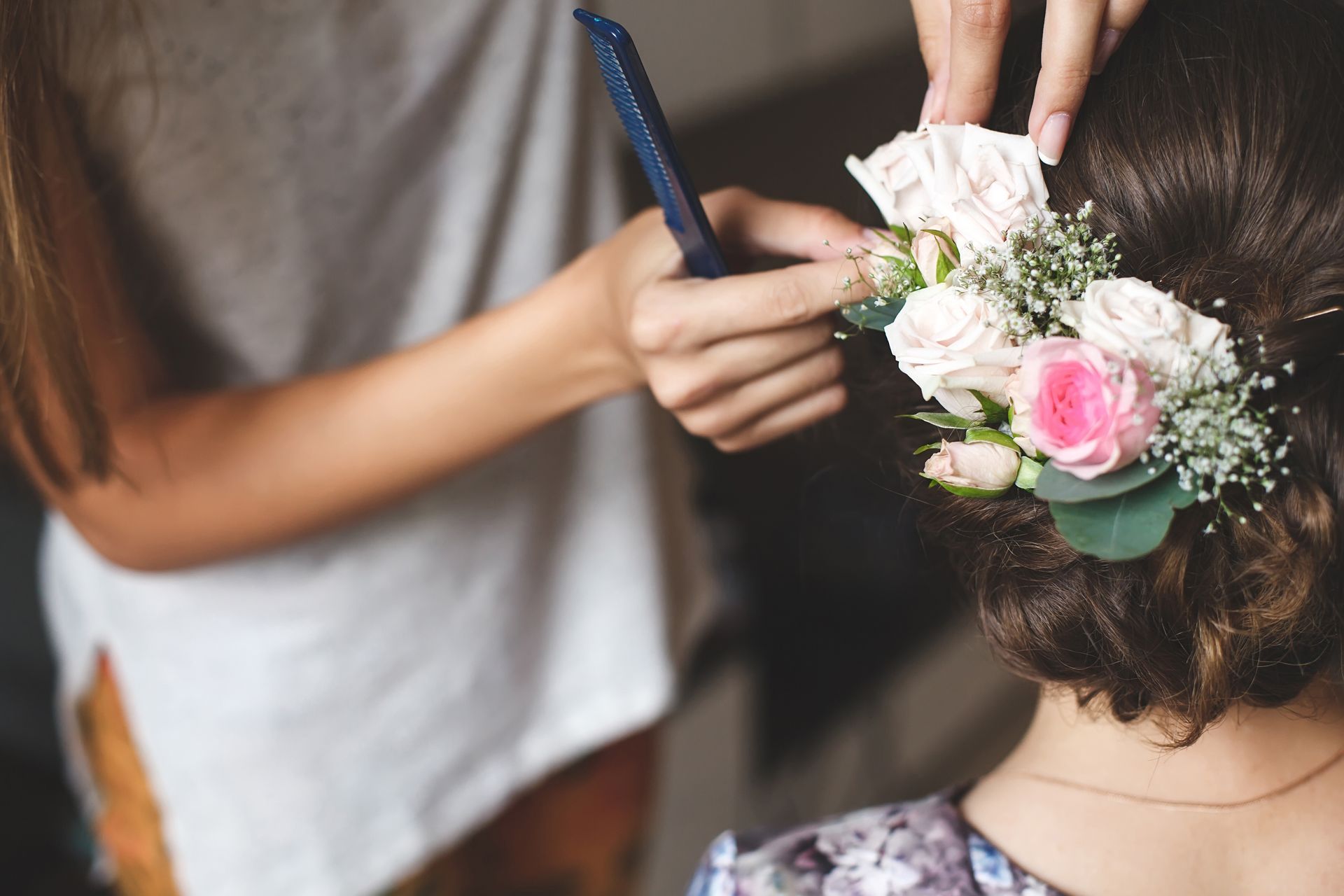 Une coiffeuse plante des fleurs dans le chignon d'une future mariée.