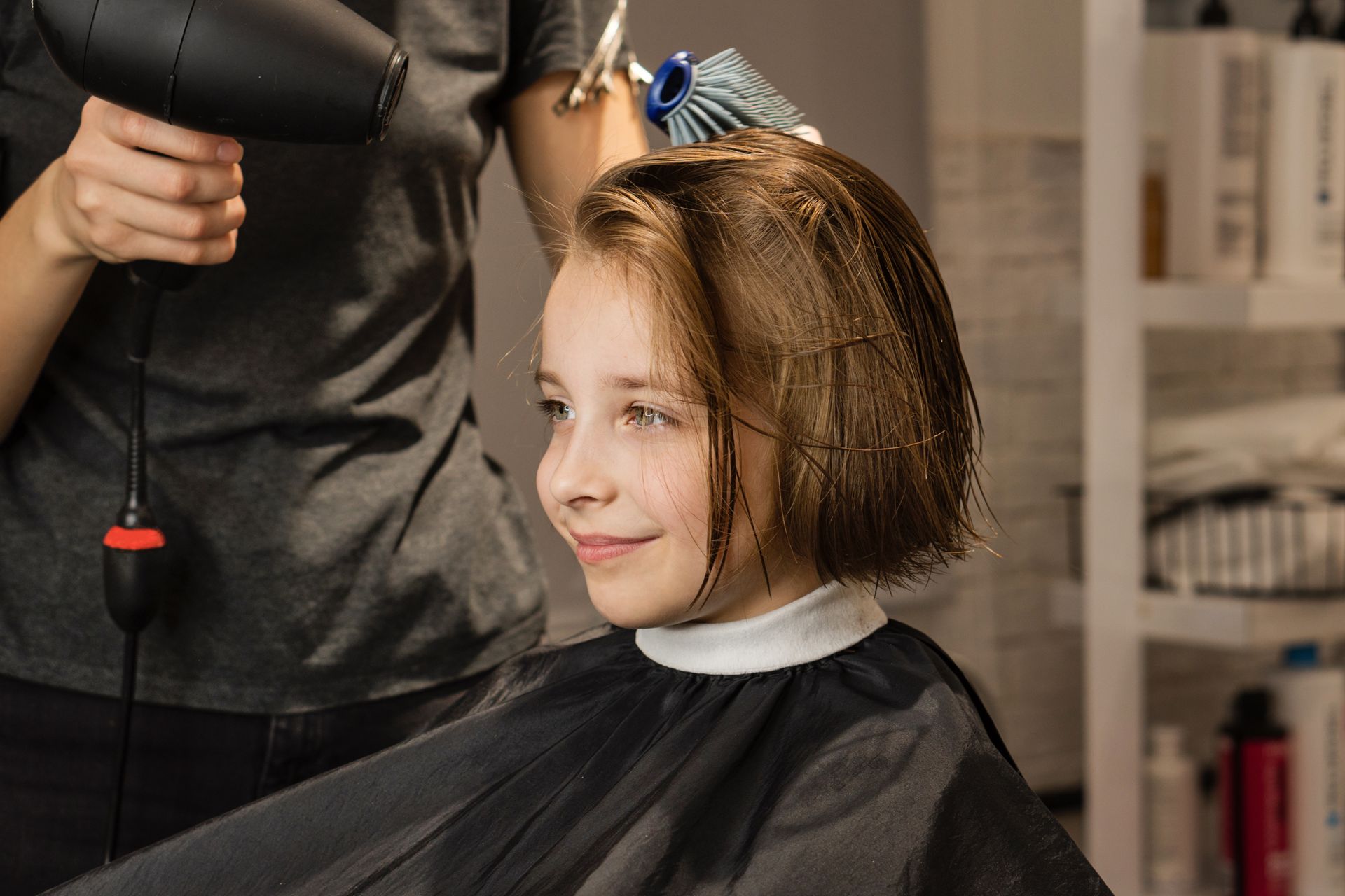 Une coiffeuse s'occupe de sécher les cheveux d'une petite fille souriante.