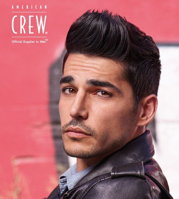 Un mannequin pose pour la marque American Crew® devant une affiche rose et blanche.