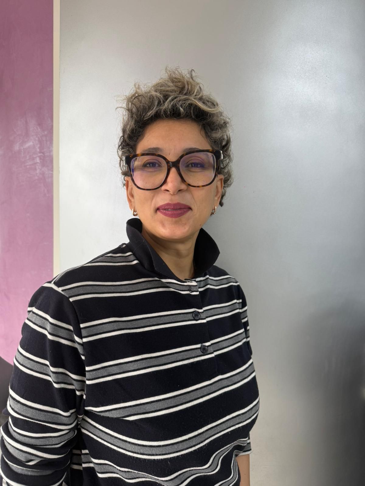 Femme portant des lunettes et un tablier, souriante dans un salon de coiffure.