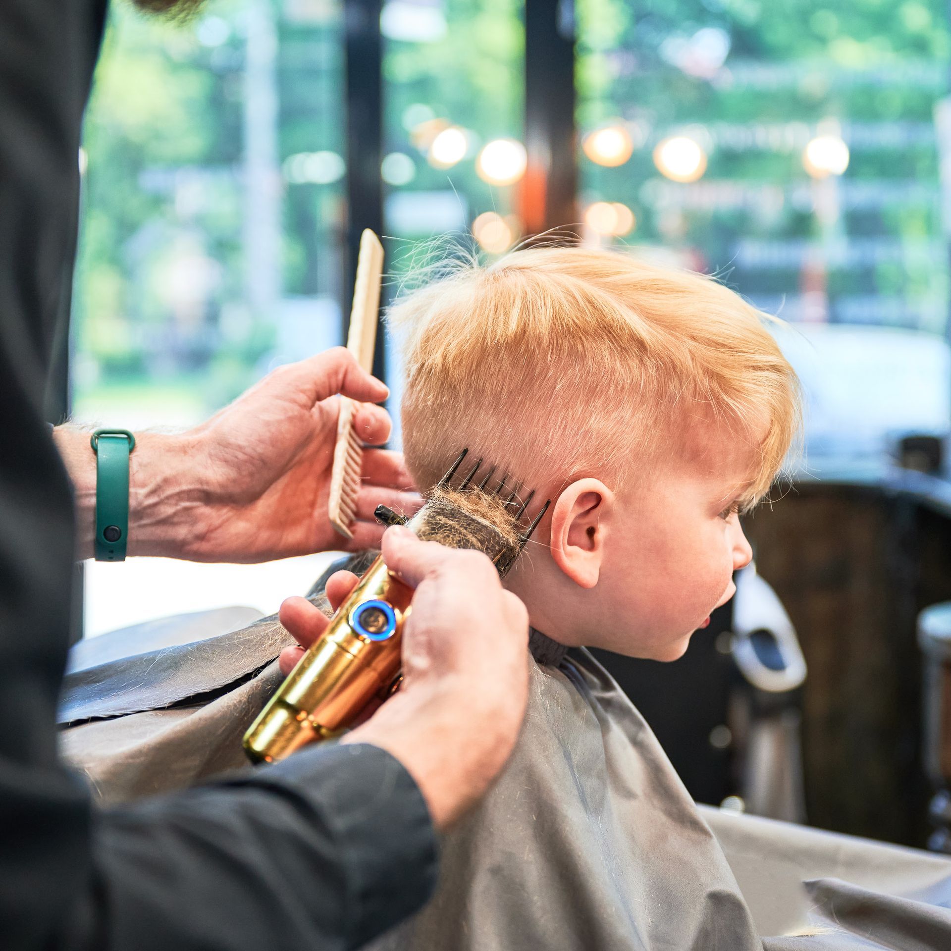 Un enfant se fait couper les cheveux à l'aide d'une tondeuse électrique et d'un peigne, à l'intérieur.