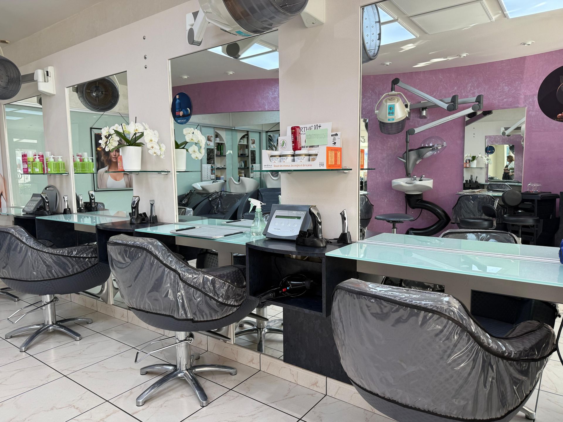 Intérieur d'un salon de coiffure avec postes de coiffage, miroirs et chaises. Murs violets et sols blancs.