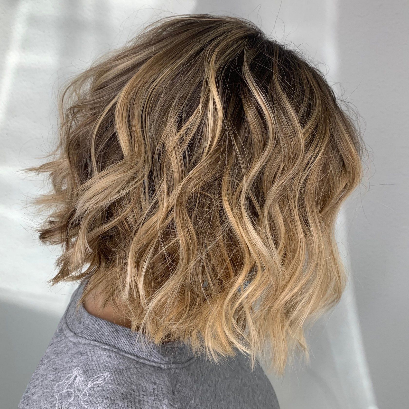 Coupe au carré ondulée blonde et brune sur une personne portant une chemise grise.