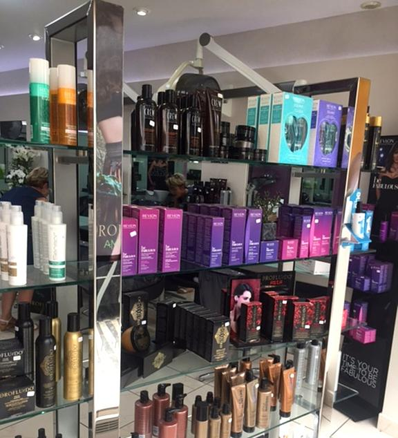 Des soins capillaires Revlon® disposés sur des étagères en verre dans un salon de coiffure.