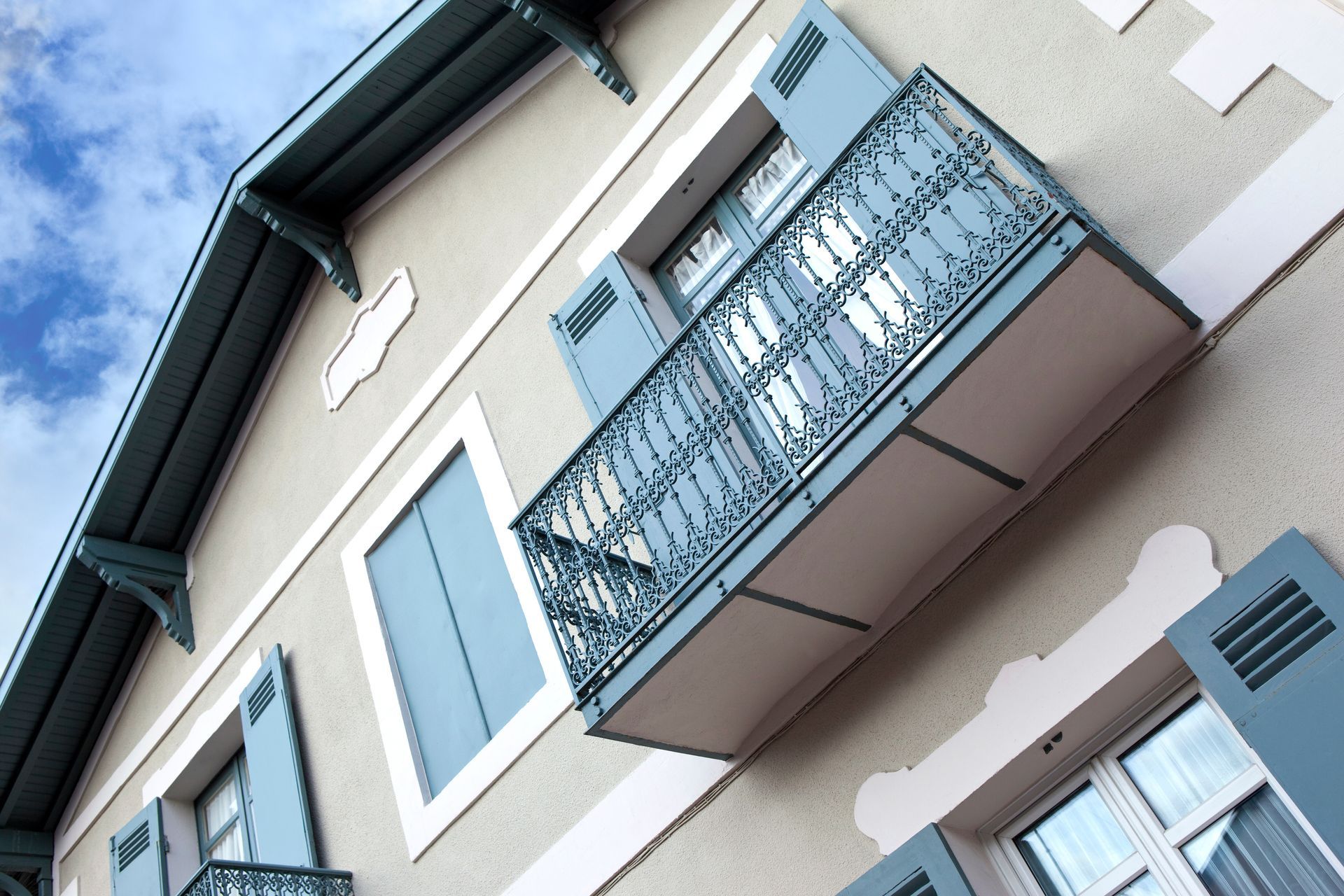 Un immeuble clair avec des volets bleus et un balcon en fer forgé.