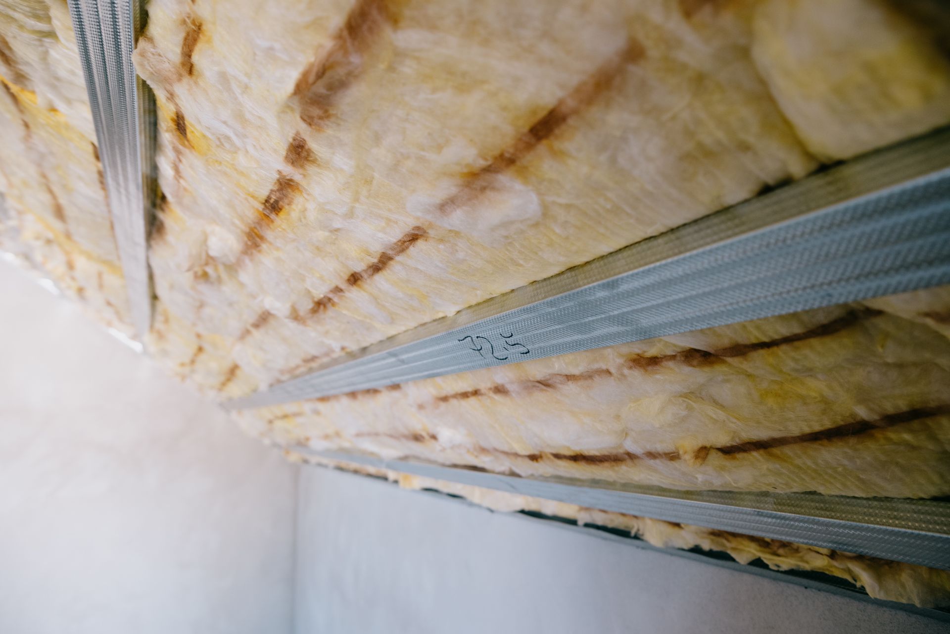 Isolation en fibre de verre jaune installée entre les montants métalliques de l'ossature du plafond.