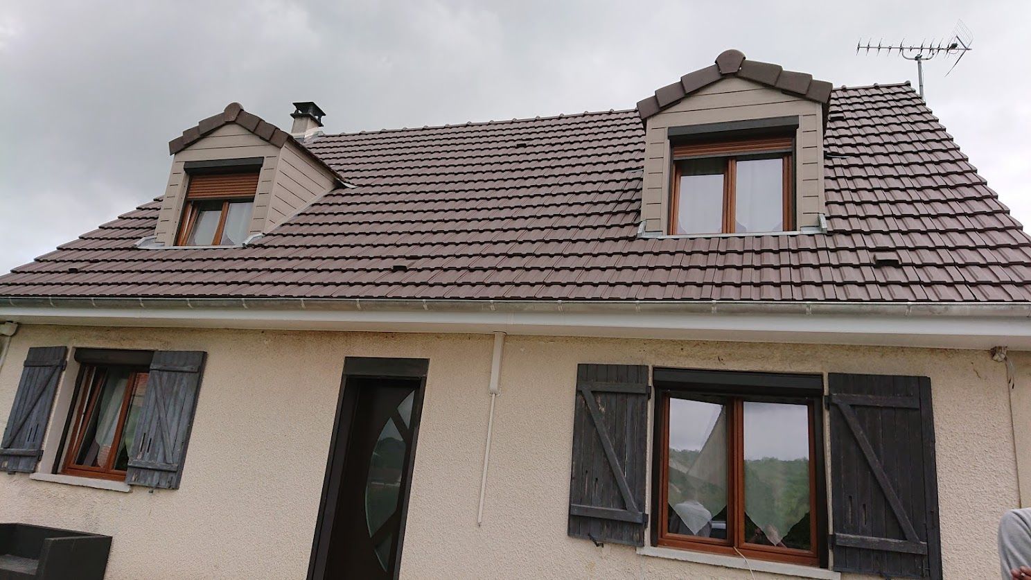 Gros plan sur un toit présentant de nouvelles tuiles en terre cuite lisses, brun rougeâtre, à côté de tuiles plus anciennes.