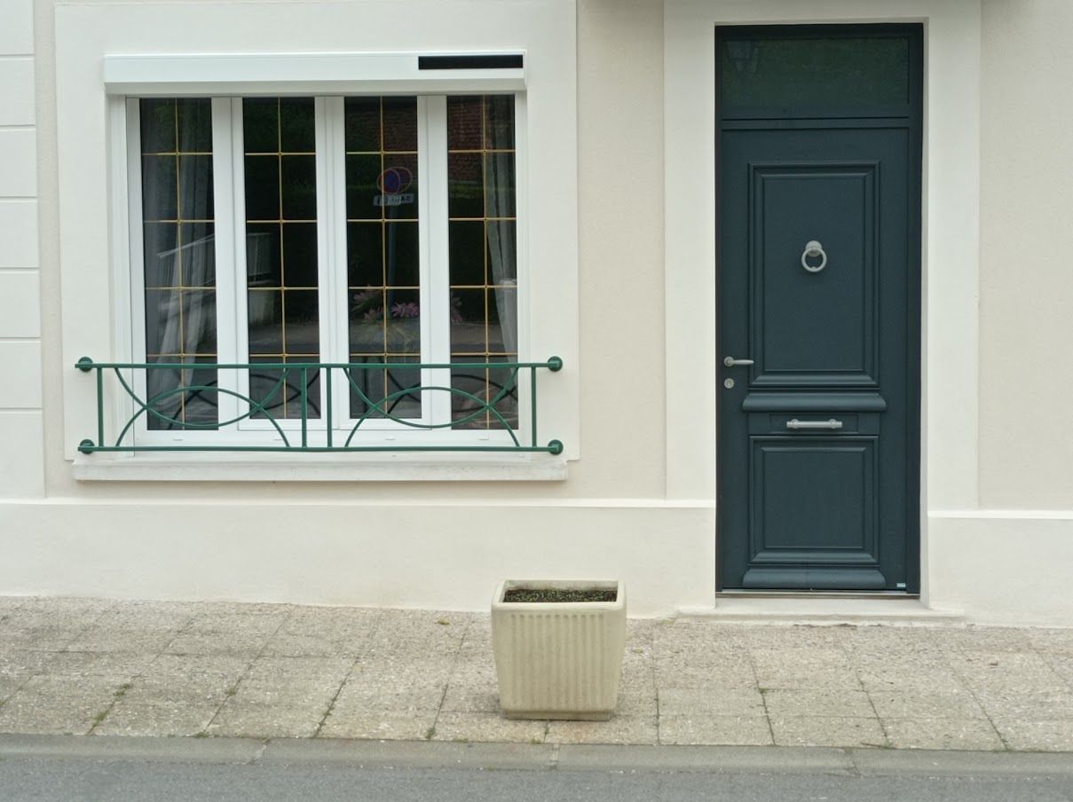 Une porte d'entrée gris foncé et une fenêtre avec une rambarde en métal vert.