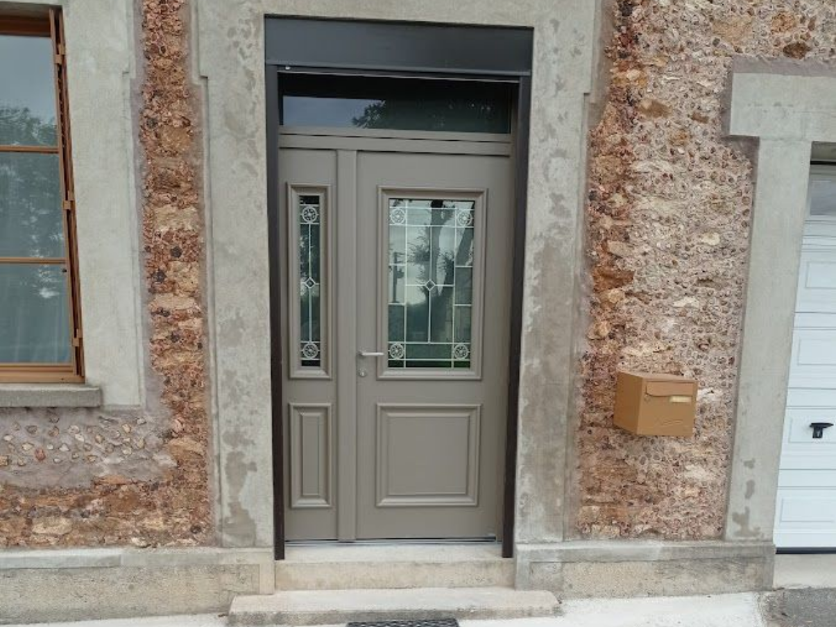 Couvreur Porte d'entrée grise avec vitre latérale, façade en pierre du bâtiment, boîte aux lettres marron.