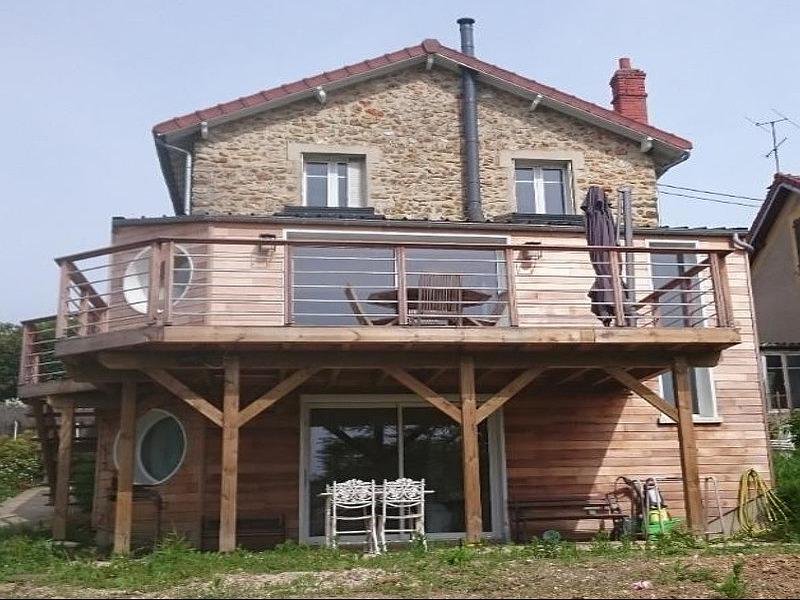 Maison &agrave; deux &eacute;tages avec terrasse en bois; fa&ccedil;ade en pierre; fen&ecirc;tres, chaises et une fen&ecirc;tre ronde.