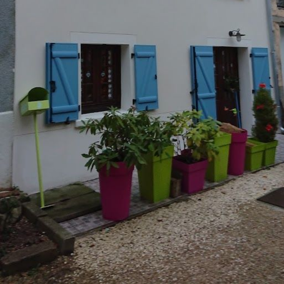 Un mur blanc avec des volets bleus, une boîte aux lettres verte et une rangée de plantes en pot colorées.