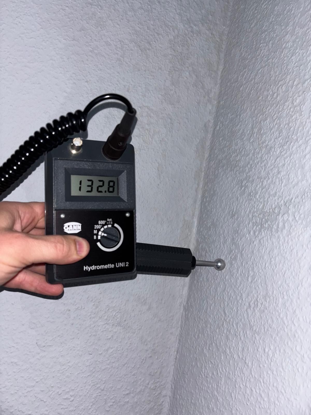 Ein Feuchtigkeitsmessgerät zeigt bei der Messung einer hellgrauen Polsteroberfläche 132,8 an.