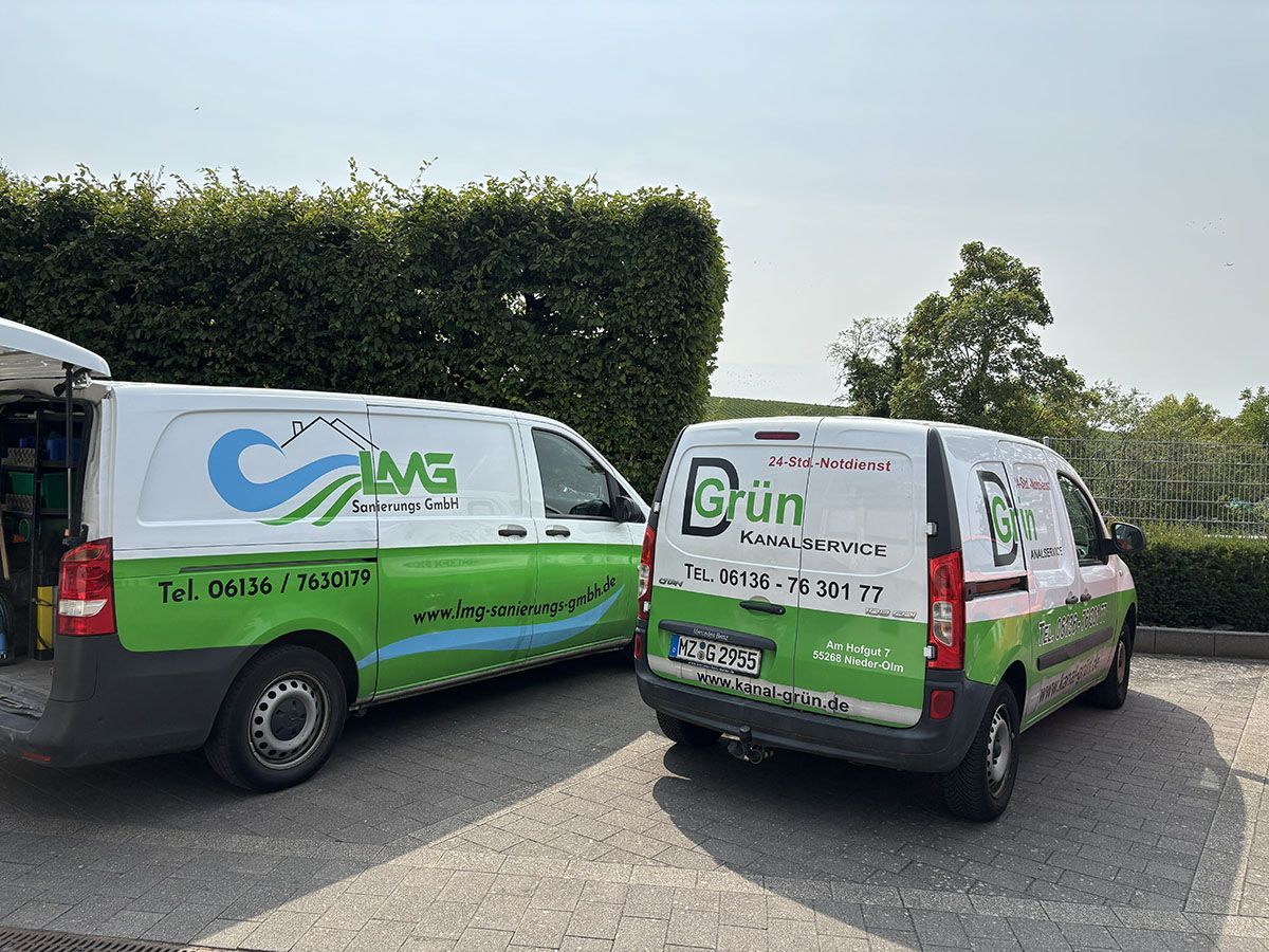 Zwei weiße Lieferwagen mit grünen Logos parkten vor einer Hecke.