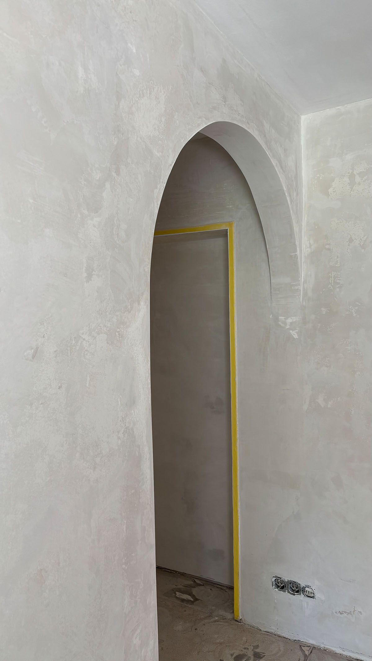 Gewölbter Türrahmen in einem Raum mit hellgrauen Wänden, gelbes Klebeband um den Türrahmen.
