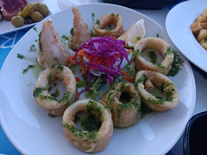 Un plato blanco cubierto con calamares fritos y verduras.