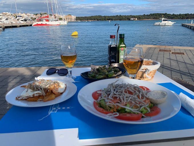 Dos platos de comida y un vaso de cerveza en una mesa junto al agua.