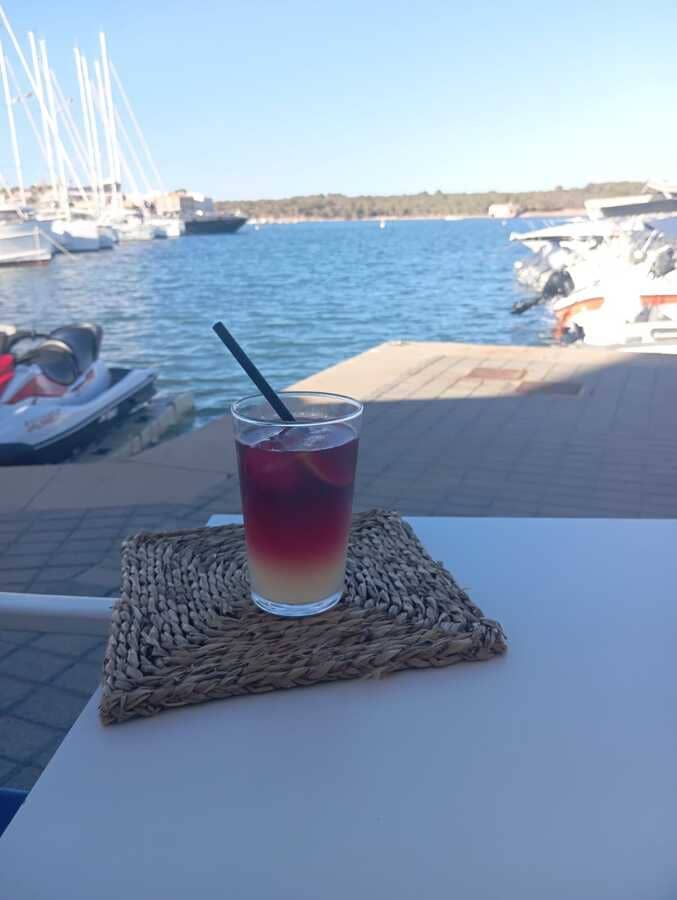 Una bebida con pajita está colocada sobre una mesa frente a un cuerpo de agua.
