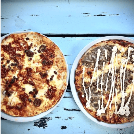 Dos pizzas en platos blancos sobre una mesa azul.