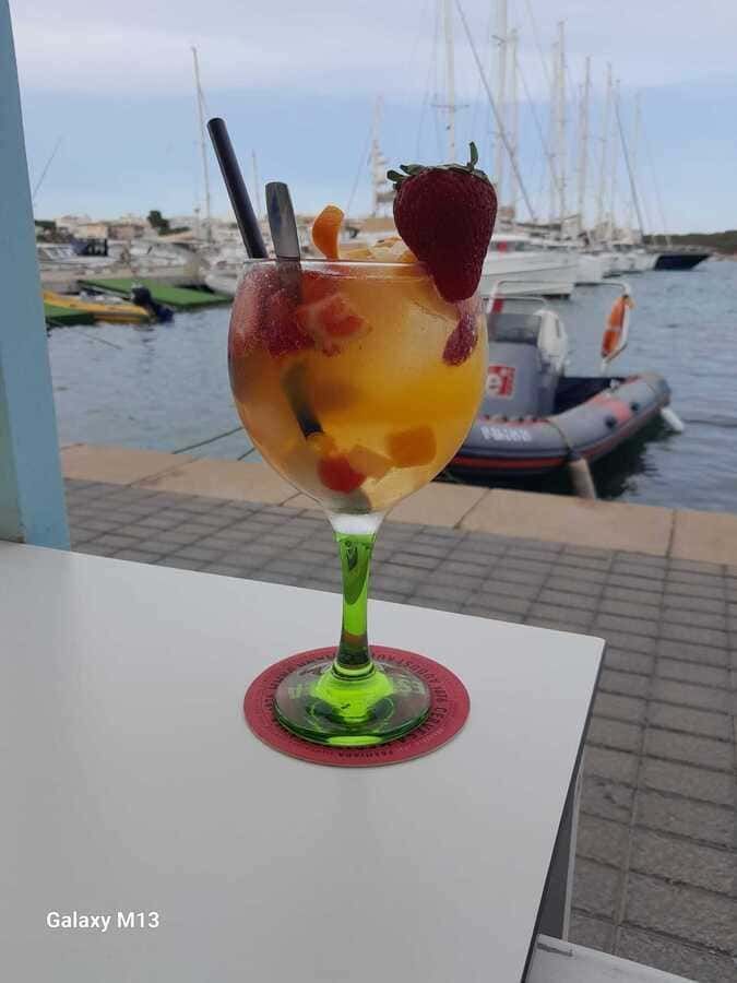 Una bebida con fresas está sobre una mesa con barcos al fondo.