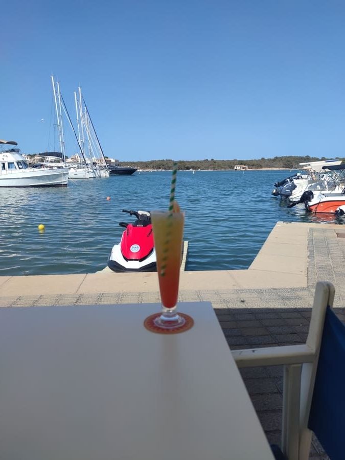 Una bebida está sobre una mesa frente a un cuerpo de agua.