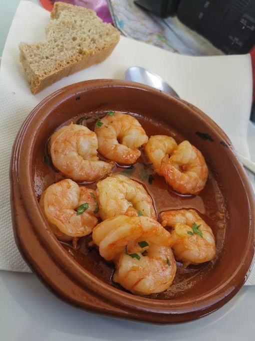 Un tazón de camarones está sobre una mesa al lado de un trozo de pan.
