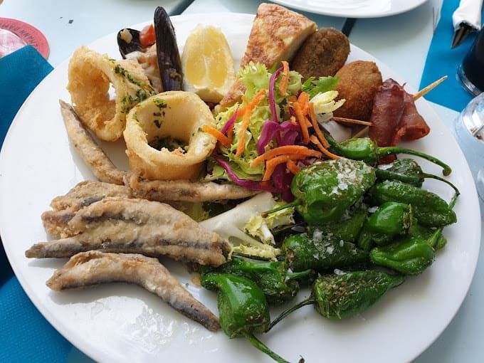 Un plato blanco cubierto con comida frita y verduras.