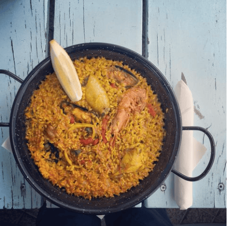 Una sartén llena de arroz y verduras con una rodaja de limón encima.