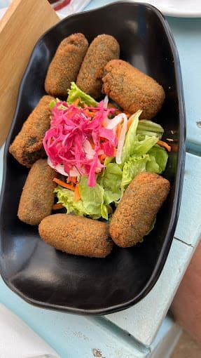 Un plato negro cubierto con comida frita y una ensalada sobre una mesa.
