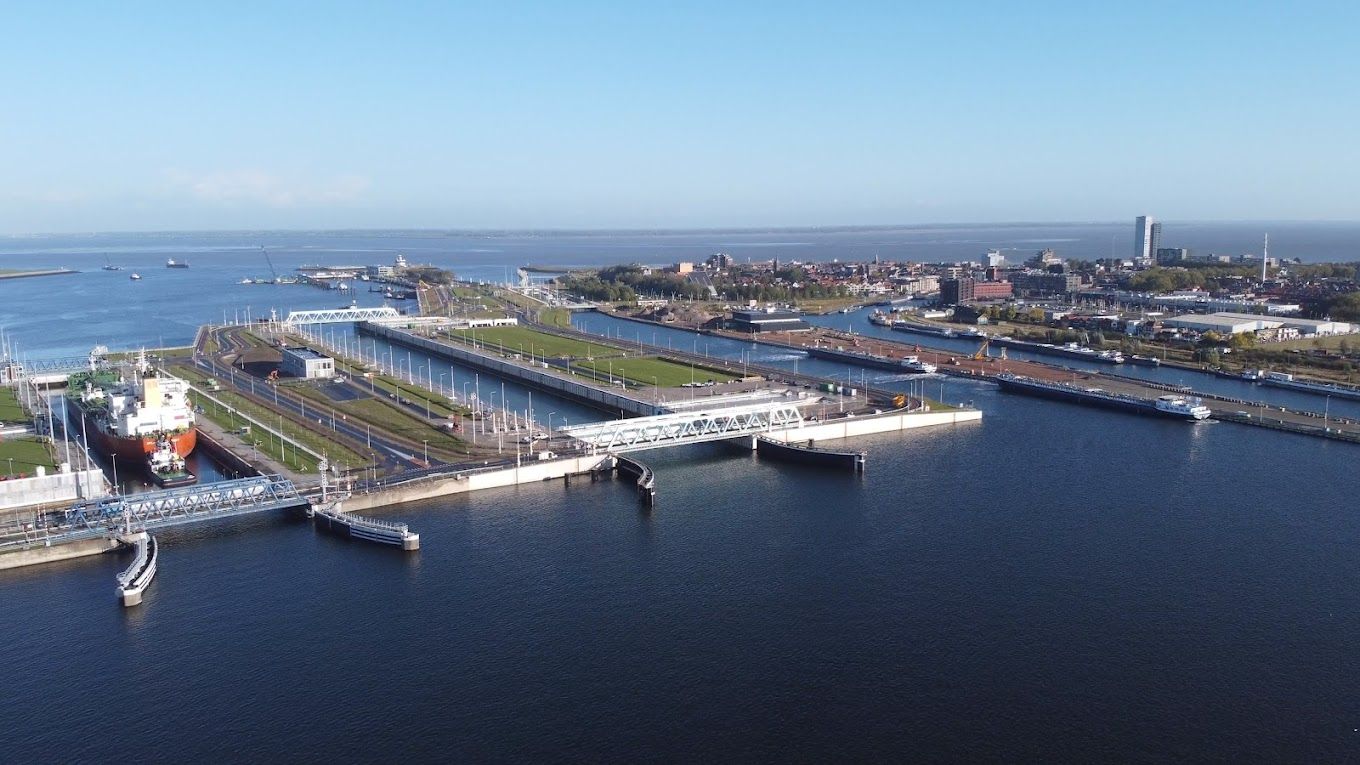 Luchtfoto van een haven met schepen, dokken en de skyline van de stad onder een helderblauwe lucht.