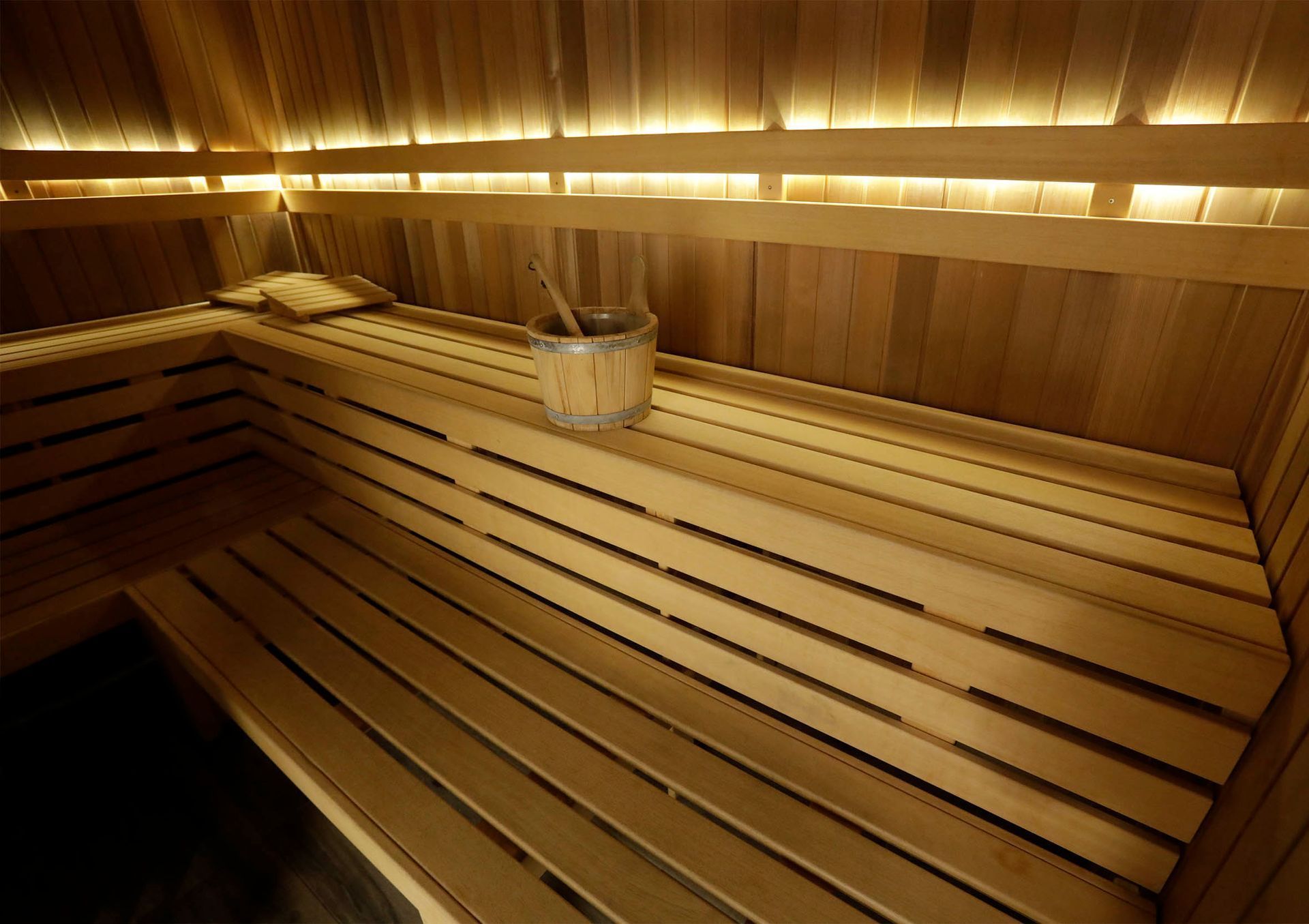 Houten sauna-interieur met banken, emmer en gedempt licht.
