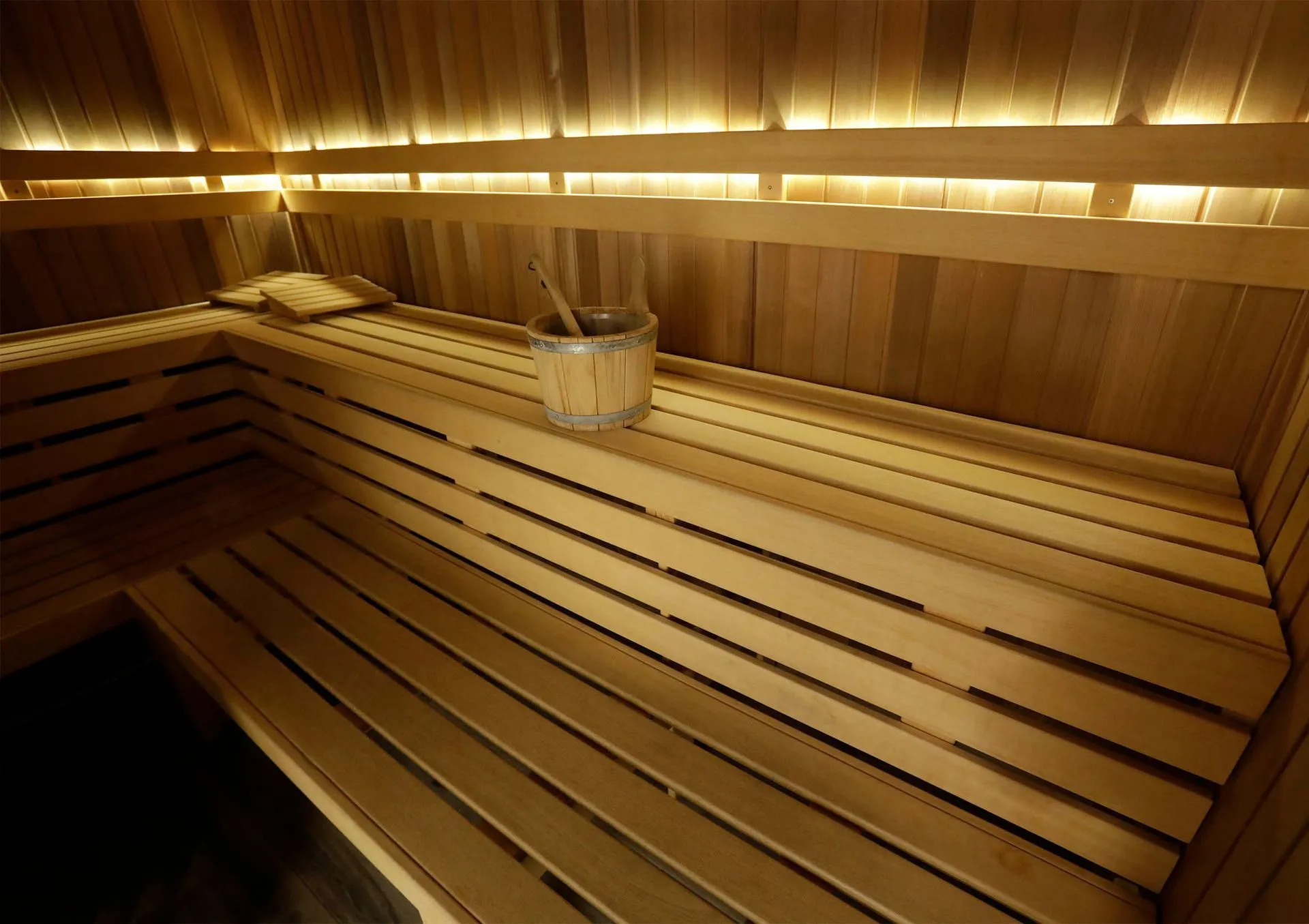 Houten sauna-interieur met banken, emmer en gedempt licht.