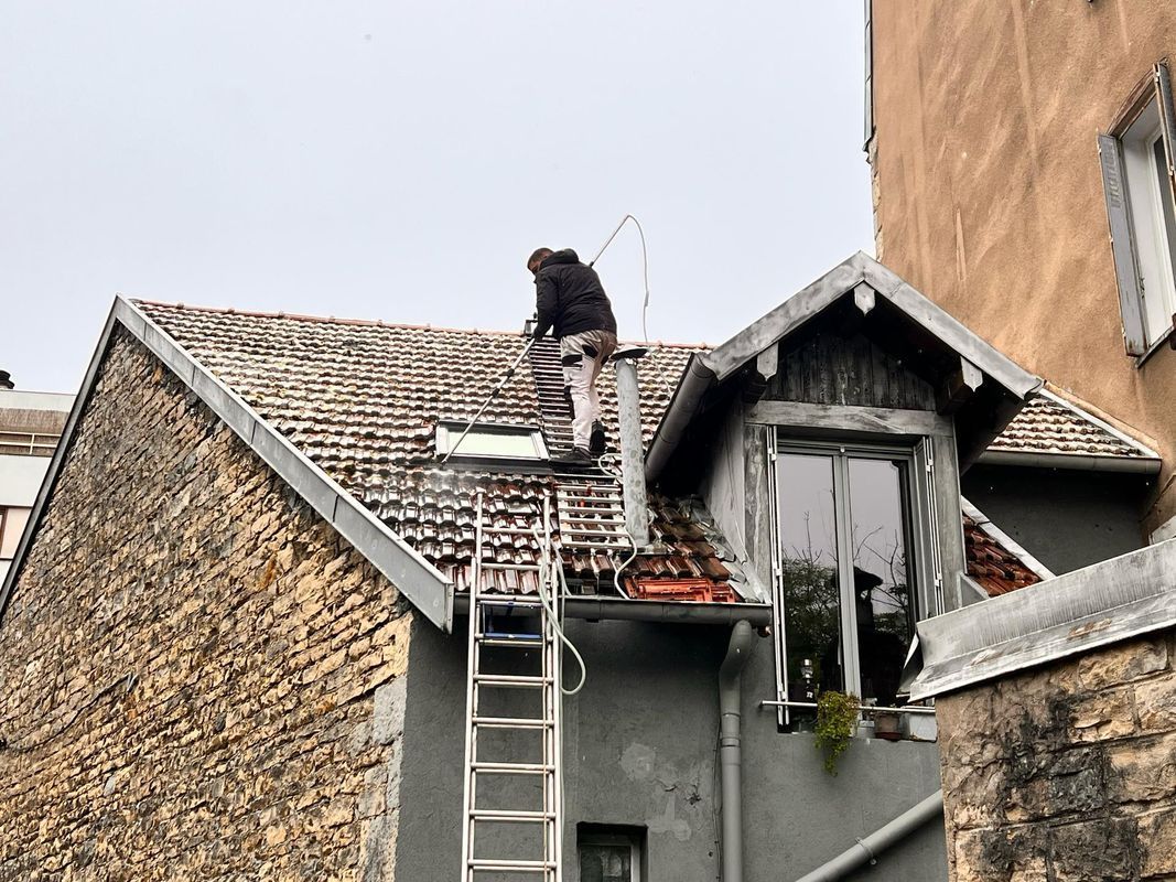 Un couvreur sur une échelle de toit nettoie une toiture.