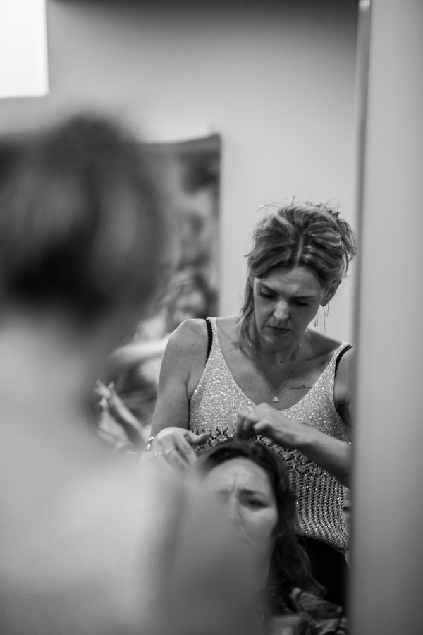 Une femme coiffe une autre femme devant un miroir. Toutes deux sont à l'intérieur, l'accent étant mis sur le travail de la coiffeuse.