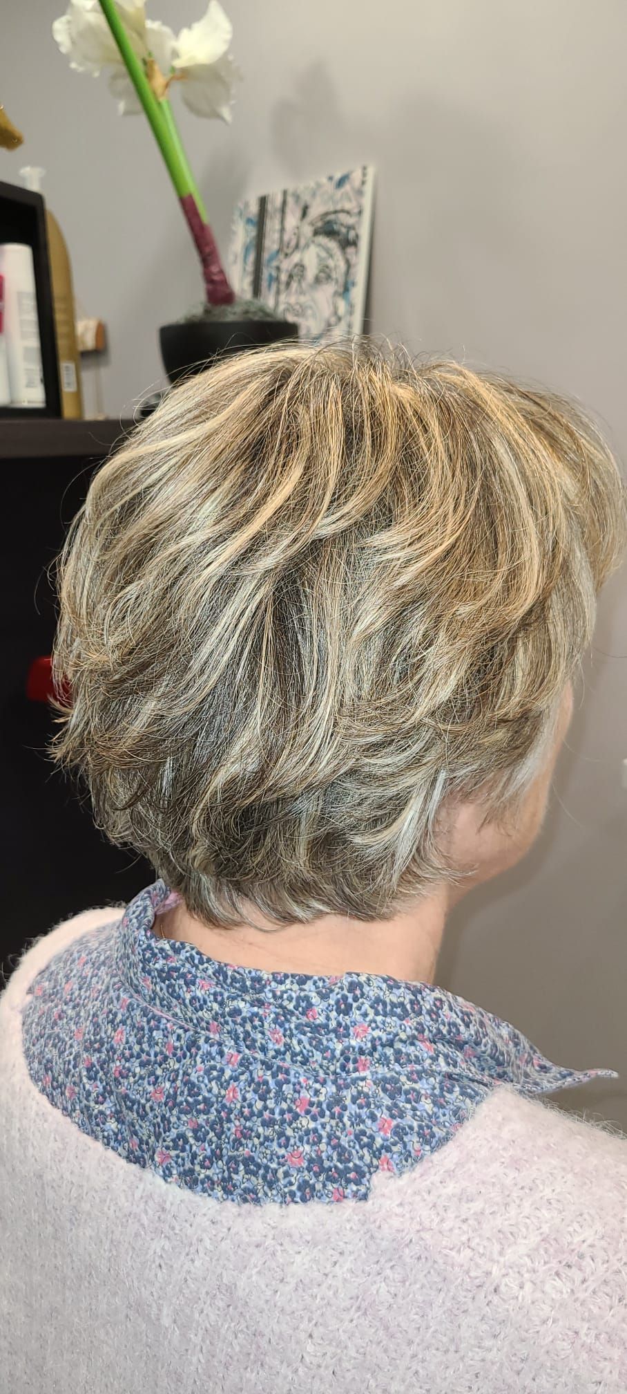 Personne aux cheveux clairs et dégradés, portant un col à motifs sur un pull rose clair.