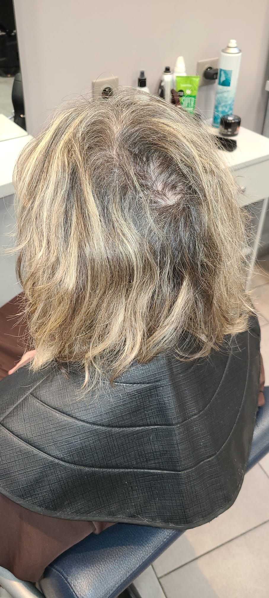 Personne aux cheveux méchés dans un salon, portant une veste noire, assise sur une chaise.