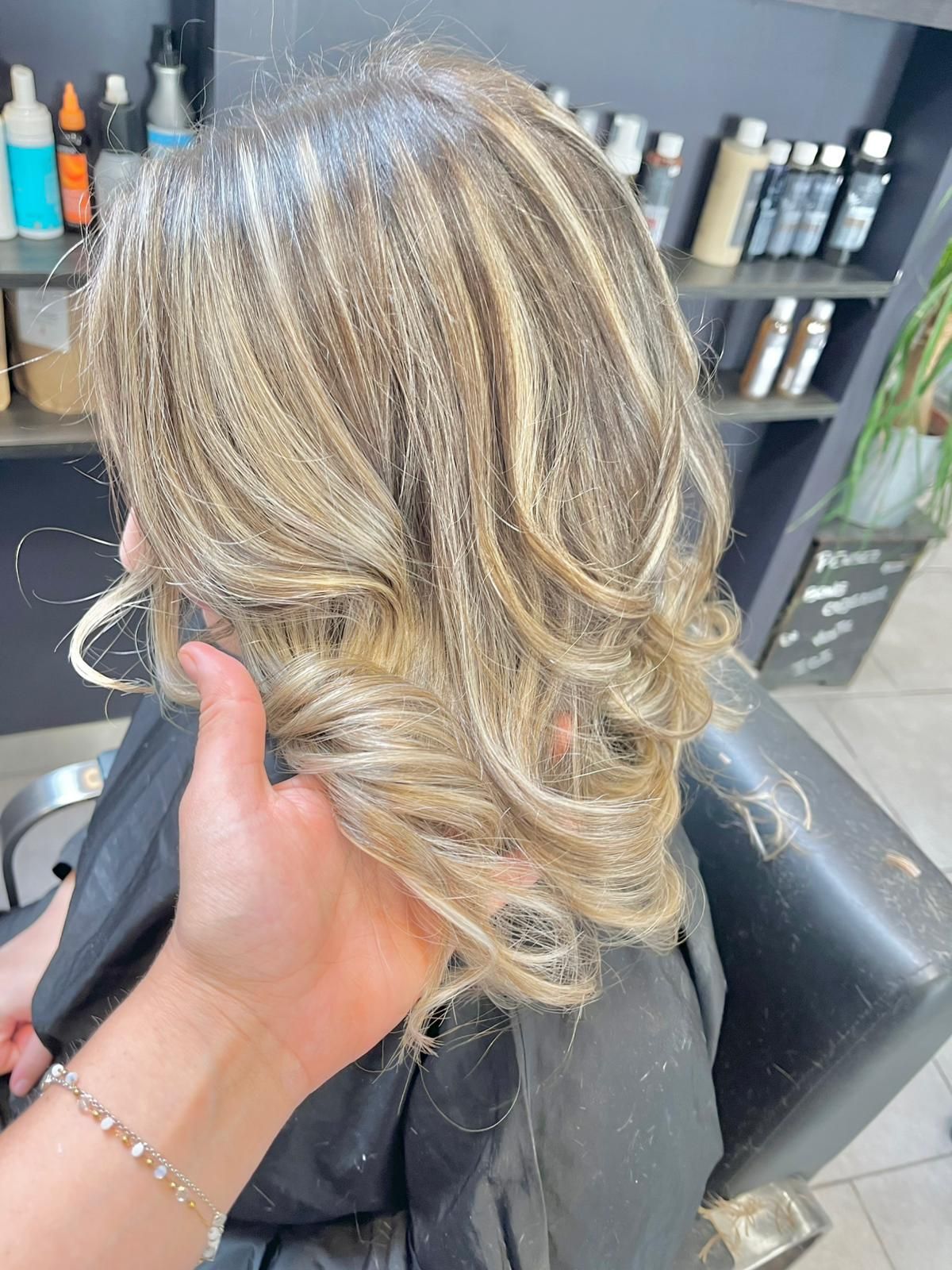 Cheveux blonds avec mèches coiffées en boucles. Main tenant les cheveux près du fauteuil, dans un salon.