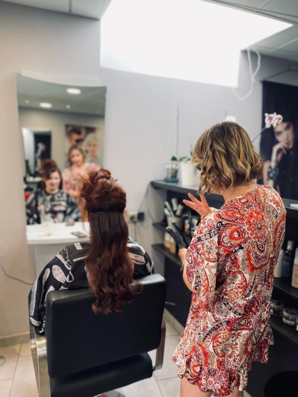 Coiffeur avec une cliente au salon. Coiffeur pointant du doigt, cliente assise, reflet dans le miroir.