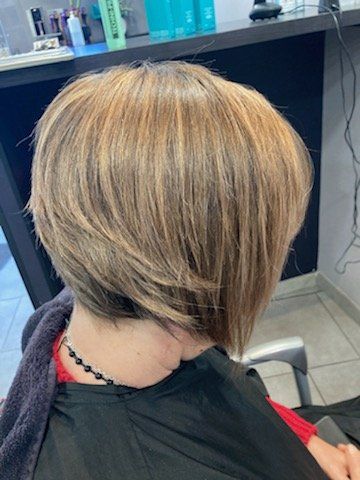 Coupe de cheveux au carré blonde et brune avec des mèches, vue de dos dans un salon.